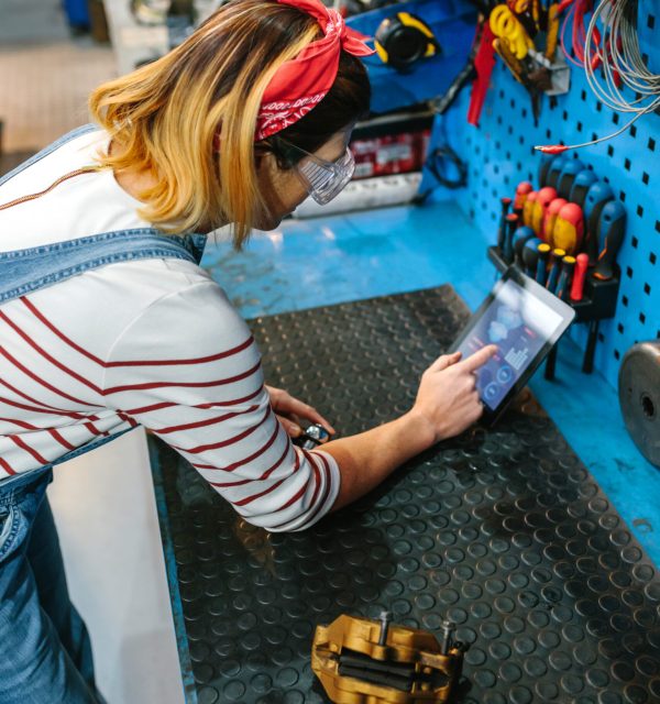 Unrecognizable mechanic woman checking disk brake on garage workbench with a diagnosis app in digital tablet